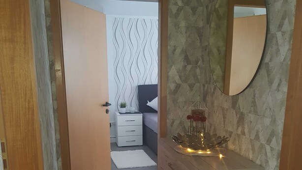 A hallway leading to a bedroom with a bed, a dresser, a mirror, and a welcome sign.