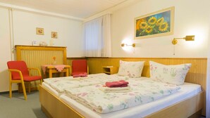 Ein Hotelzimmer mit einem Holzbett, zwei roten Stühlen, einem kleinen Tisch und einem Sonnenblumenbild an der Wand.