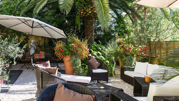 An outdoor patio with wicker furniture, a white umbrella, and a statue. - idealsejour (Cannes)