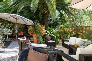 An outdoor patio with wicker furniture, a white umbrella, and a statue. - idealsejour (Cannes)