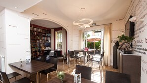 A modern hotel lobby with a central seating area, a bookshelf, and a dining area with tables and chairs. - idealsejour (Cannes)