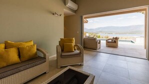 A modern living room with a sofa, two armchairs, and a view of a pool and mountains.