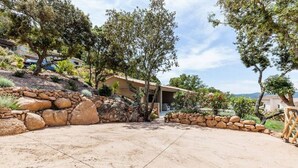 A house with a stone retaining wall, a paved driveway, and a backyard with trees and shrubs.