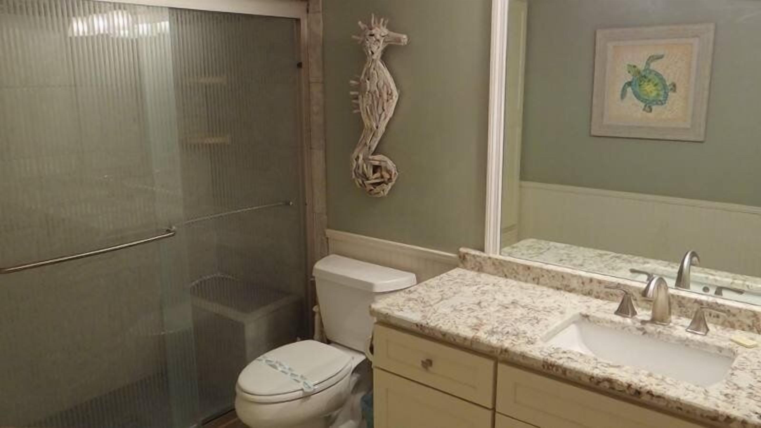 Un baño con cabina de ducha de vidrio, inodoro, lavamanos con espejo y un adorno de caballito de mar en la pared.