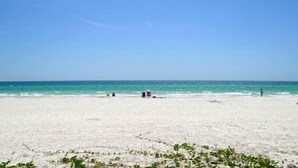 Une vaste plage de sable fin, sous un ciel bleu dégagé et une mer calme.