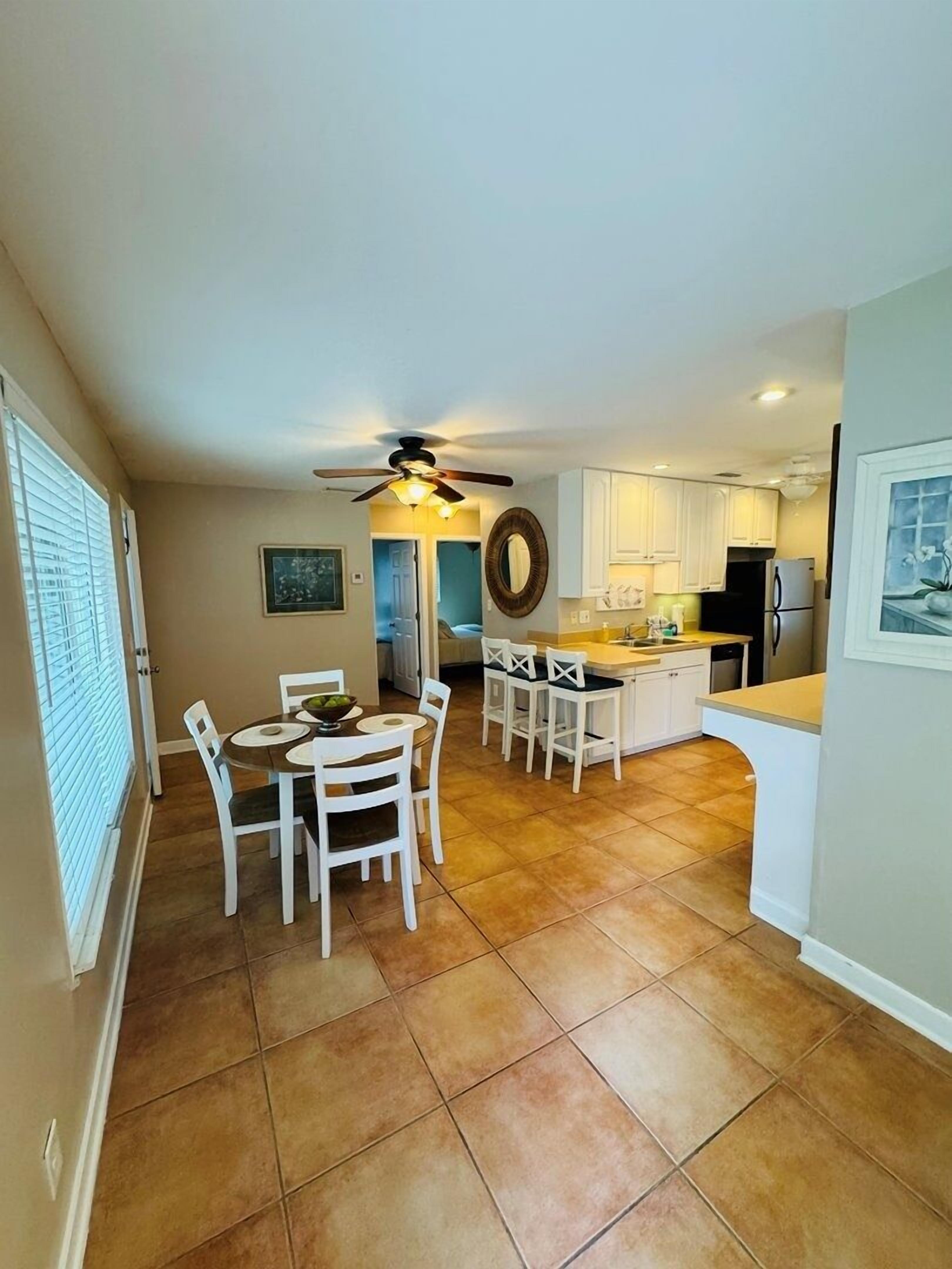 A spacious kitchen with white cabinets, a dining area with white chairs, and a ceiling fan.
