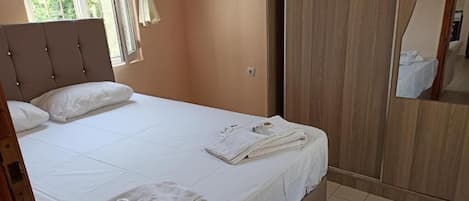 A bedroom with a bed, white linens, a wooden wardrobe, and a window with curtains.