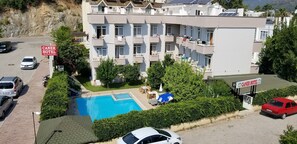 A multi-story hotel with a swimming pool, outdoor seating, and a sign indicating the hotel name. - Caner Hotel (Kemer)