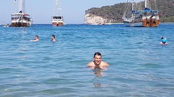 Une mer d’un bleu profond où l’on aperçoit plusieurs voiliers et des personnes qui nagent.