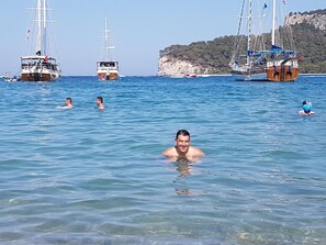 A clear blue sea with several sailboats and people swimming. - Caner Hotel (Kemer)