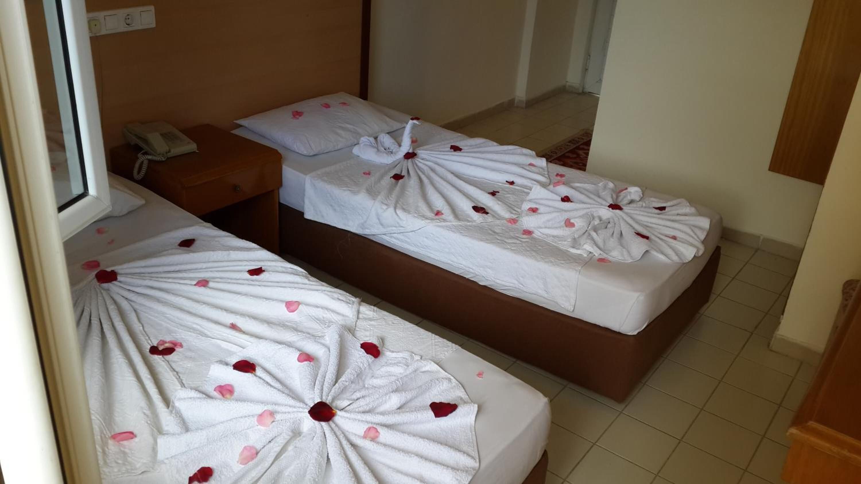 Deux lits simples avec du linge de lit blanc et des pétales de rose, une table de chevet et un téléphone.