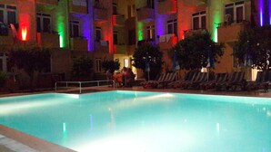 Una piscina con zona de borde, rodeada de edificios con iluminación colorida.