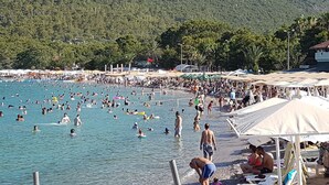 Una playa concurrida, gente nadando y tomando el sol, sombrillas y sillas de playa.