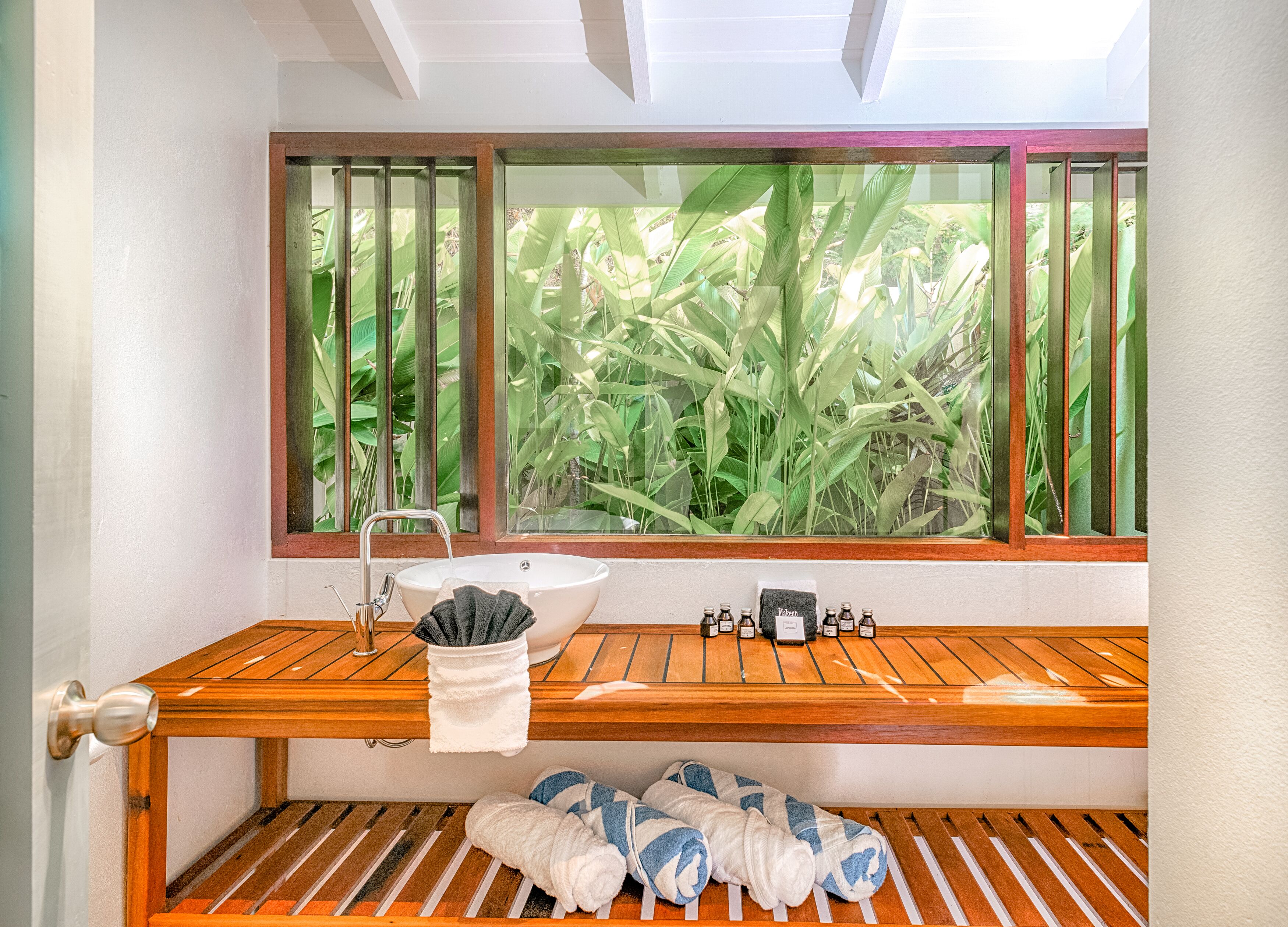 A bathroom with a wooden vanity, a white sink, and a window with a view of green foliage.