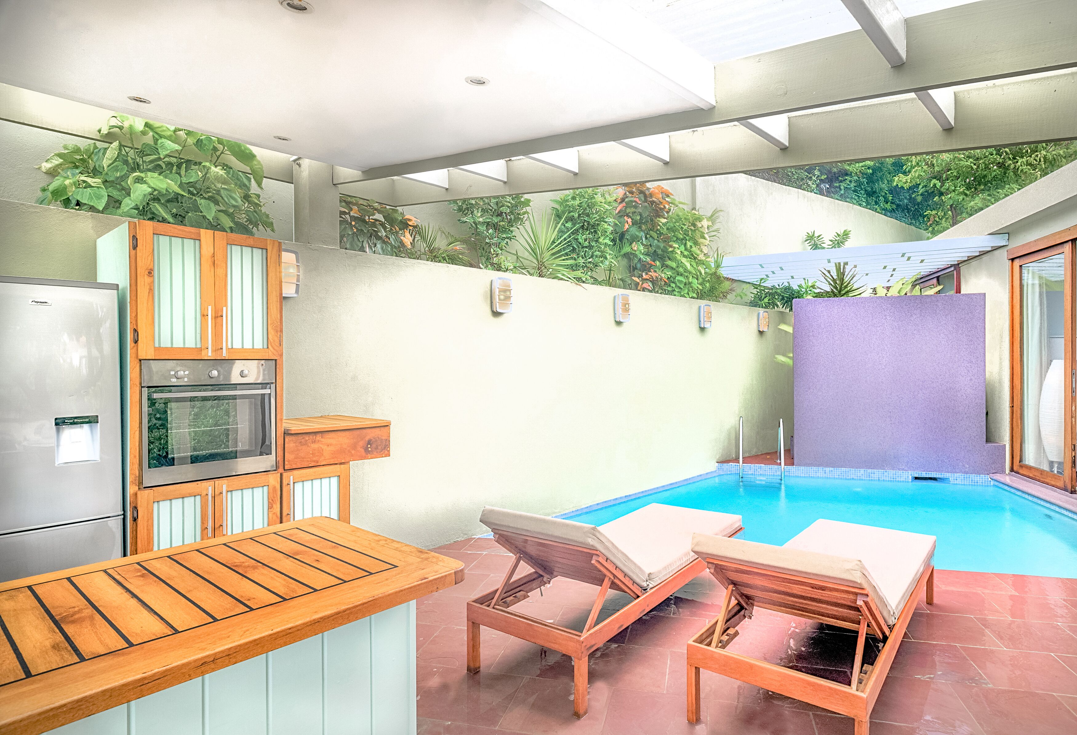 A modern kitchen with a built-in oven, a wooden countertop, and a small pool area with lounge chairs.