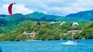 A coastal scene with a person windsurfing, houses on a hillside, and a clear sky.