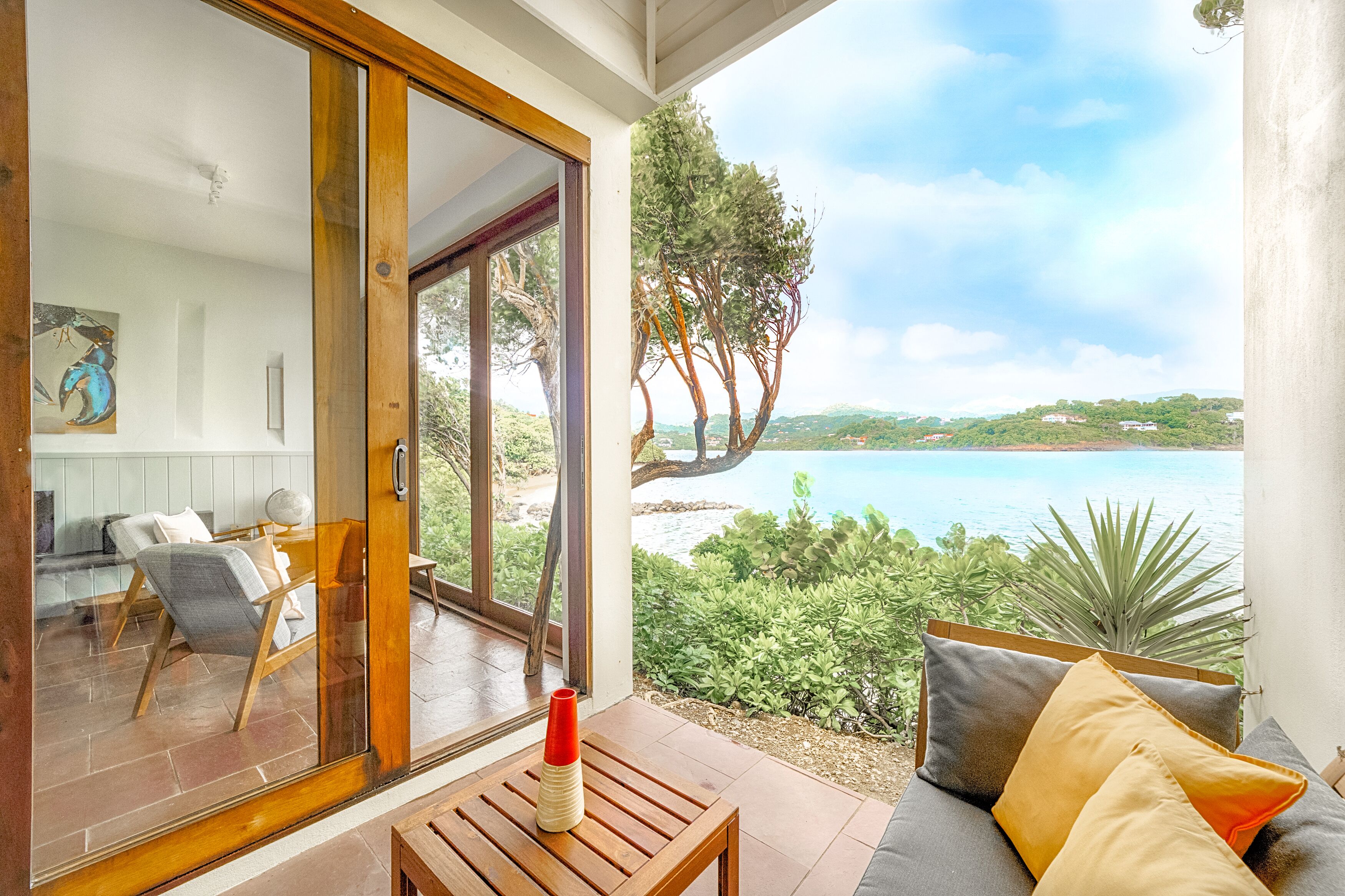 Un balcón con vistas al mar, una mesa de madera y un sofá con cojines.