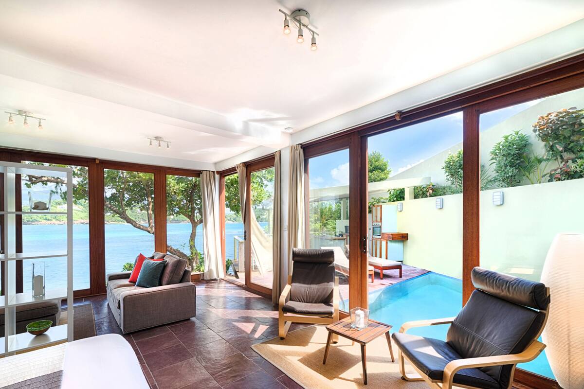 A spacious room with a large window, a pool, and a seating area with a table and chairs.