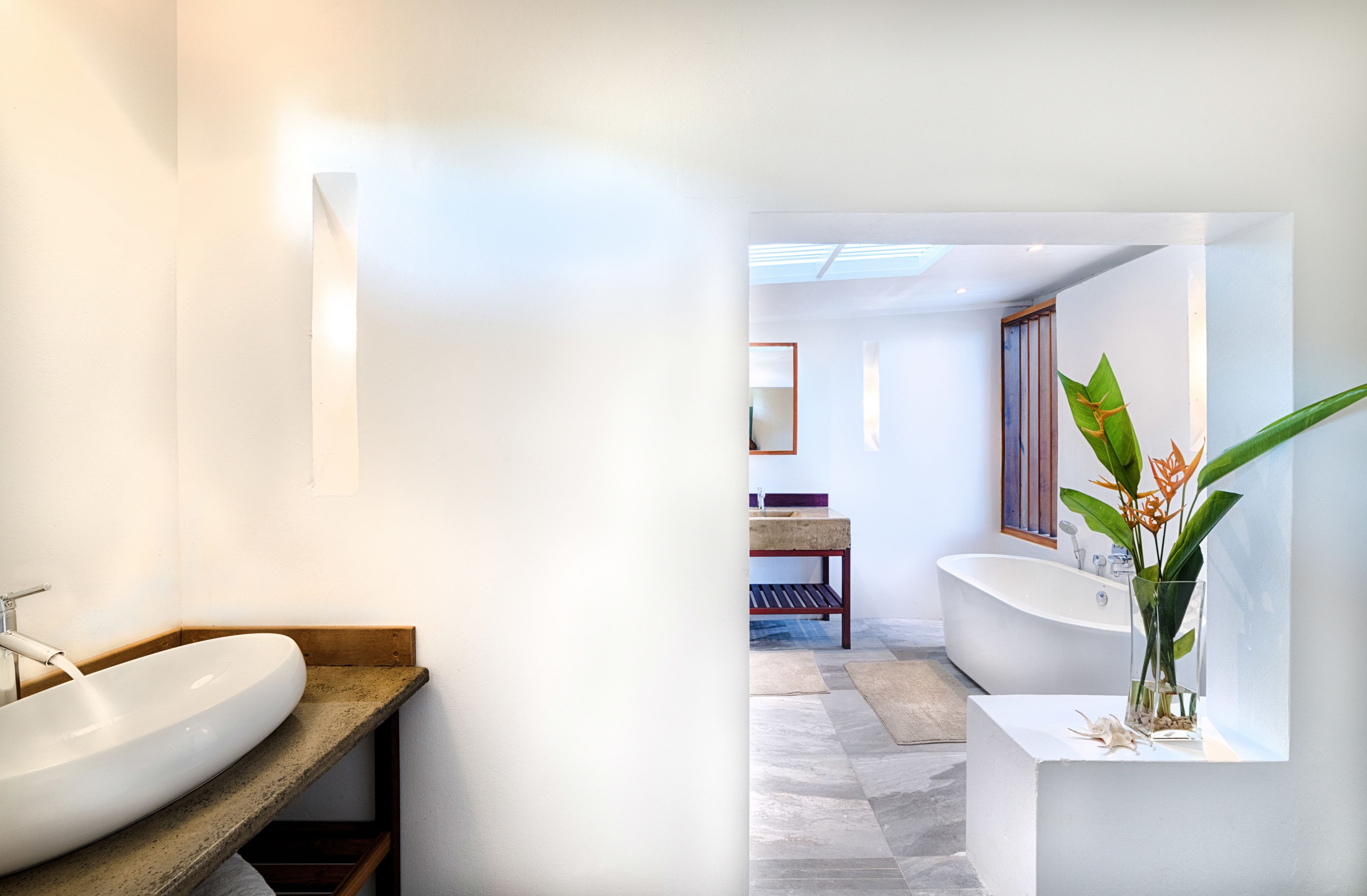 Ein modernes Badezimmer mit einem großen, weißen Waschbecken, einer Holzbank, einer freistehenden Badewanne und einer Topfpflanze.