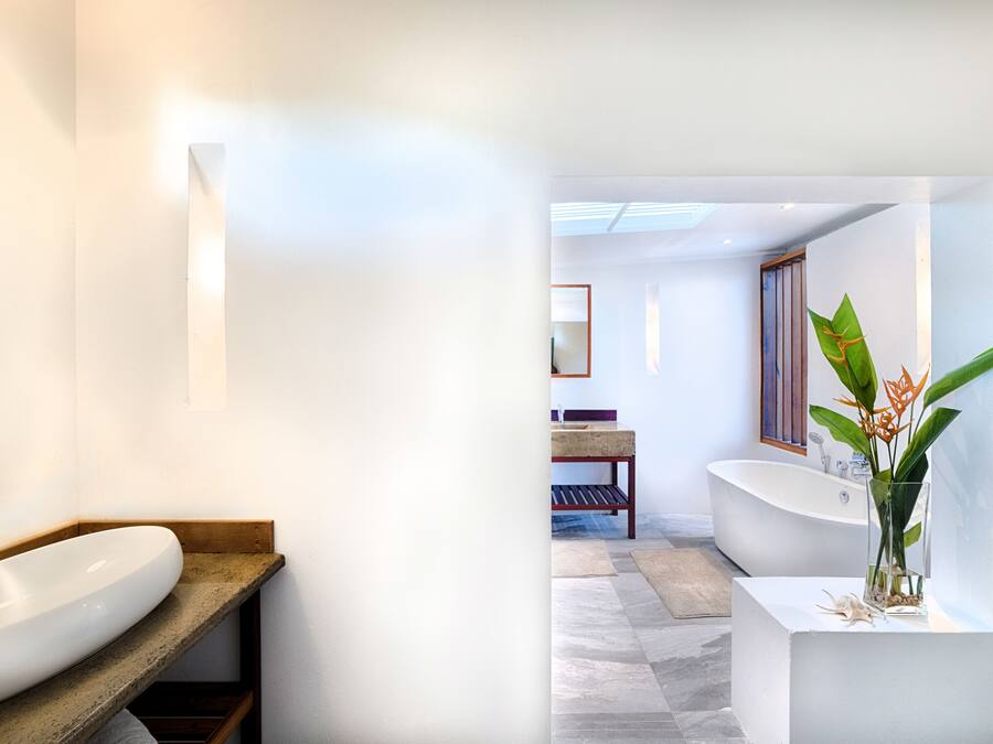 Ein modernes Badezimmer mit einem großen, weißen Waschbecken, einer Holzbank, einer freistehenden Badewanne und einer Topfpflanze.