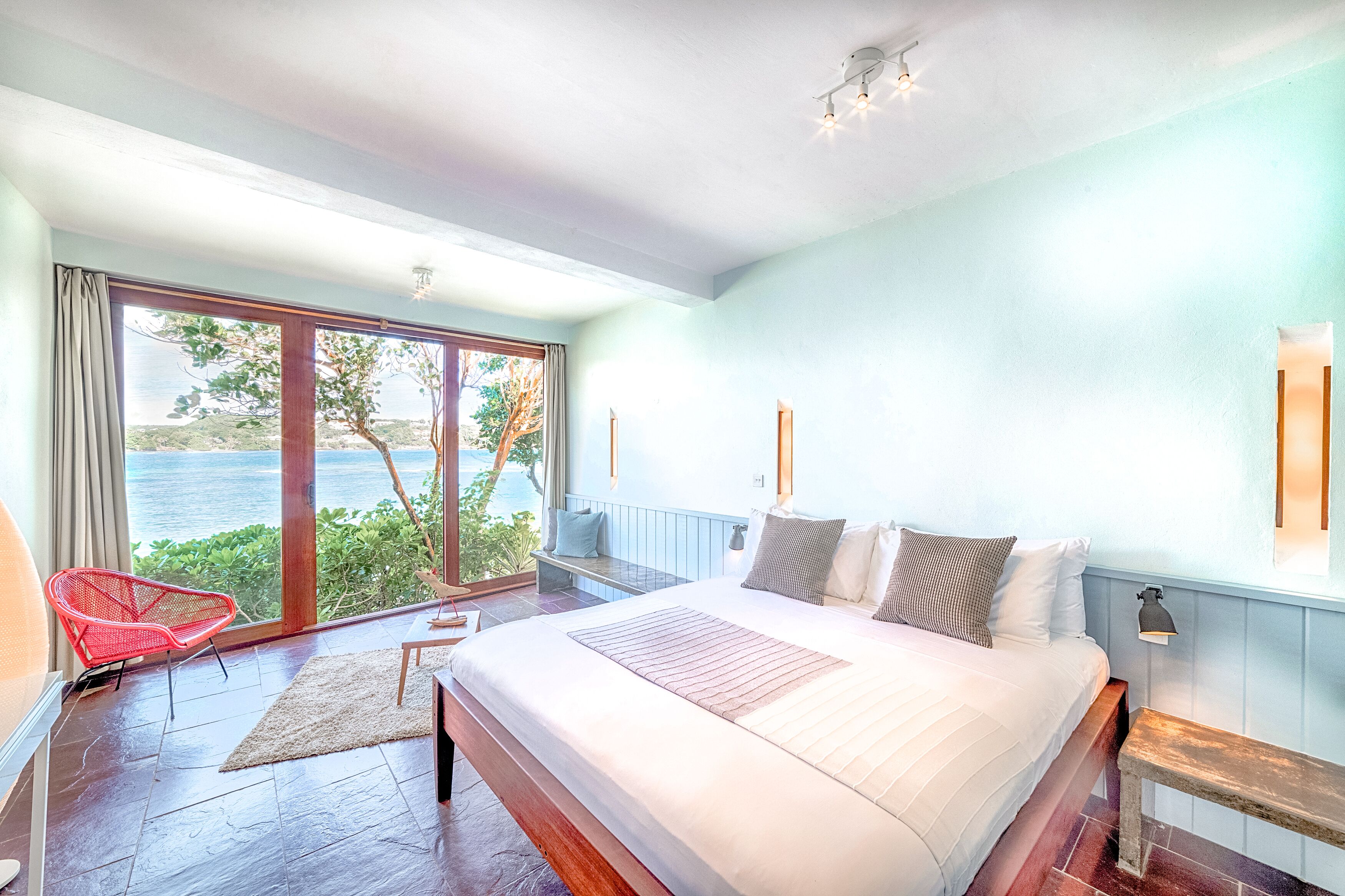 Une chambre avec un grand lit, un fauteuil rouge et une vue sur la mer.