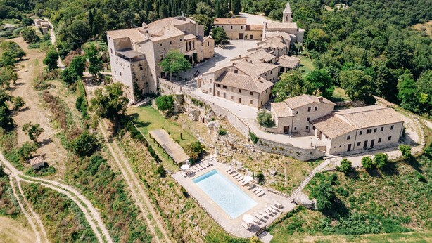 An aerial view of a historic stone building complex with multiple structures, a swimming pool, and surrounding greenery. - Castello di Titignano (Orvieto)