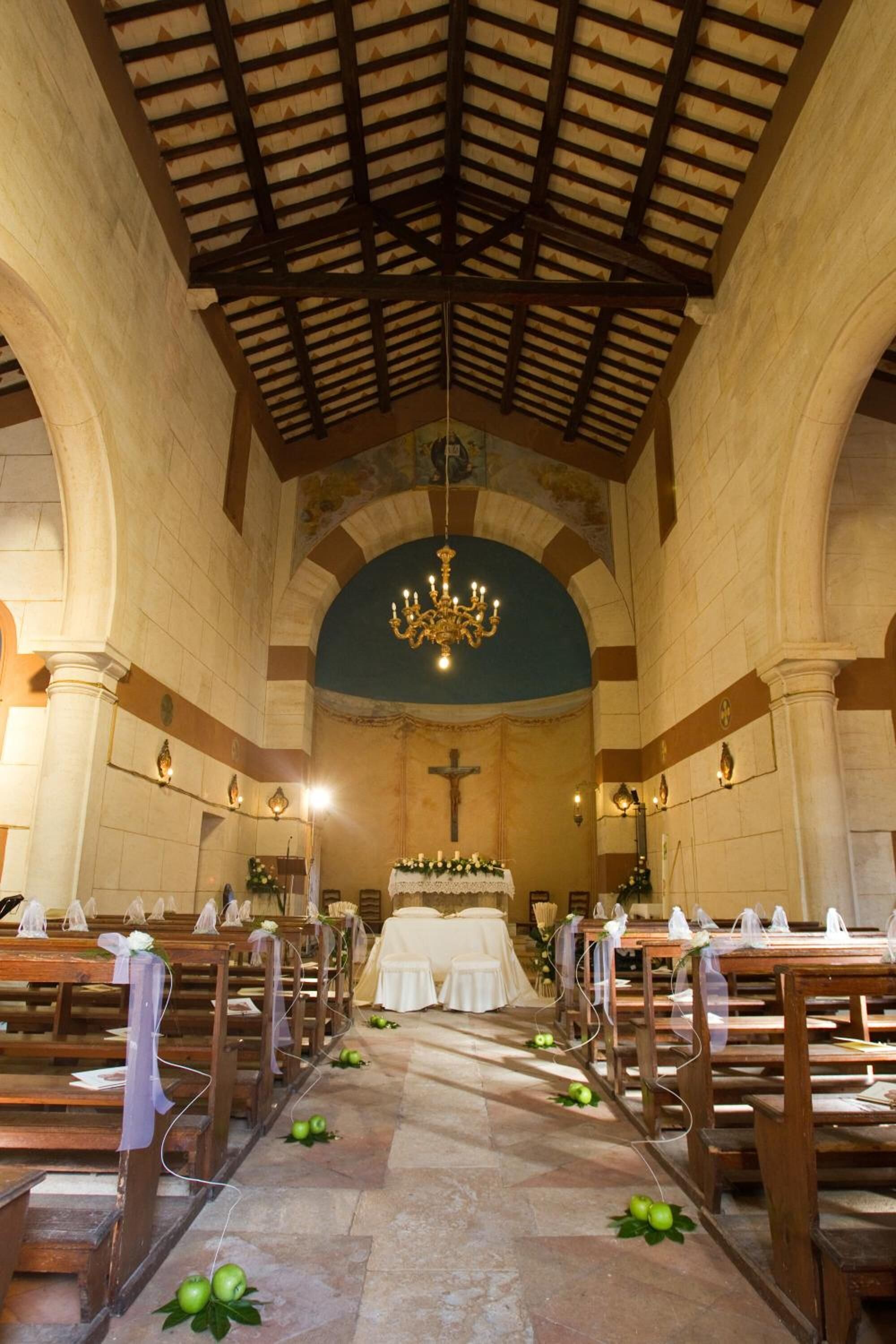 Interior de una iglesia con bancos de madera, un altar central y una lámpara de araña.