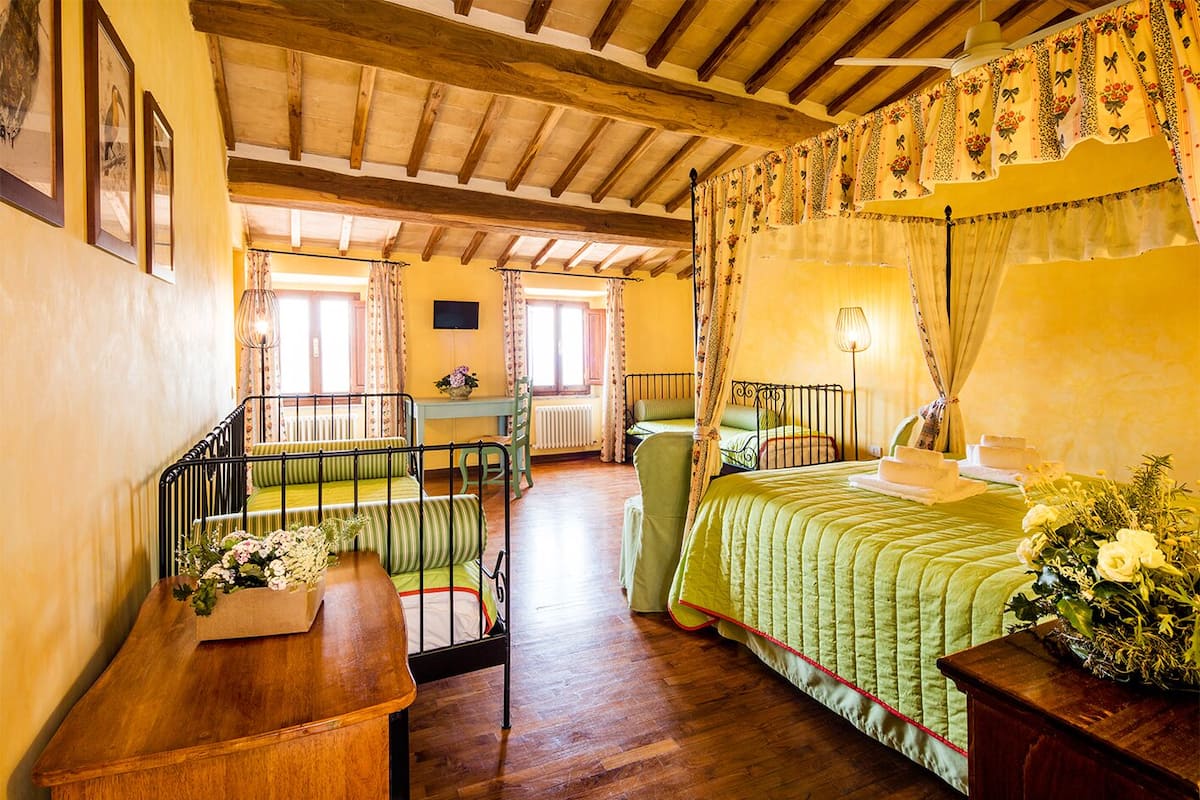 A room with a wooden ceiling, a bed with green bedding, a table with a vase of flowers, and a chair.