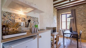 Una cocina con estufa moderna, microondas y pileta. Se observa una mesa de comedor con sillas y una pared de piedra al fondo.