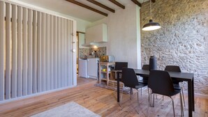 Un comedor con una mesa y sillas de madera, una pared de piedra y una cocina al fondo.