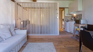 Un salón moderno con un sofá blanco, suelo de madera y un separador con persianas verticales.