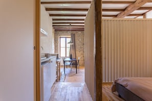 A narrow hallway leading to a bedroom with a wooden ceiling and stone walls.