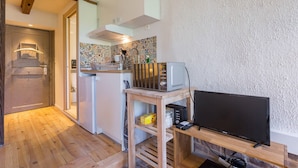 Una cocina compacta con microondas, tostadora y televisor sobre un soporte de madera.