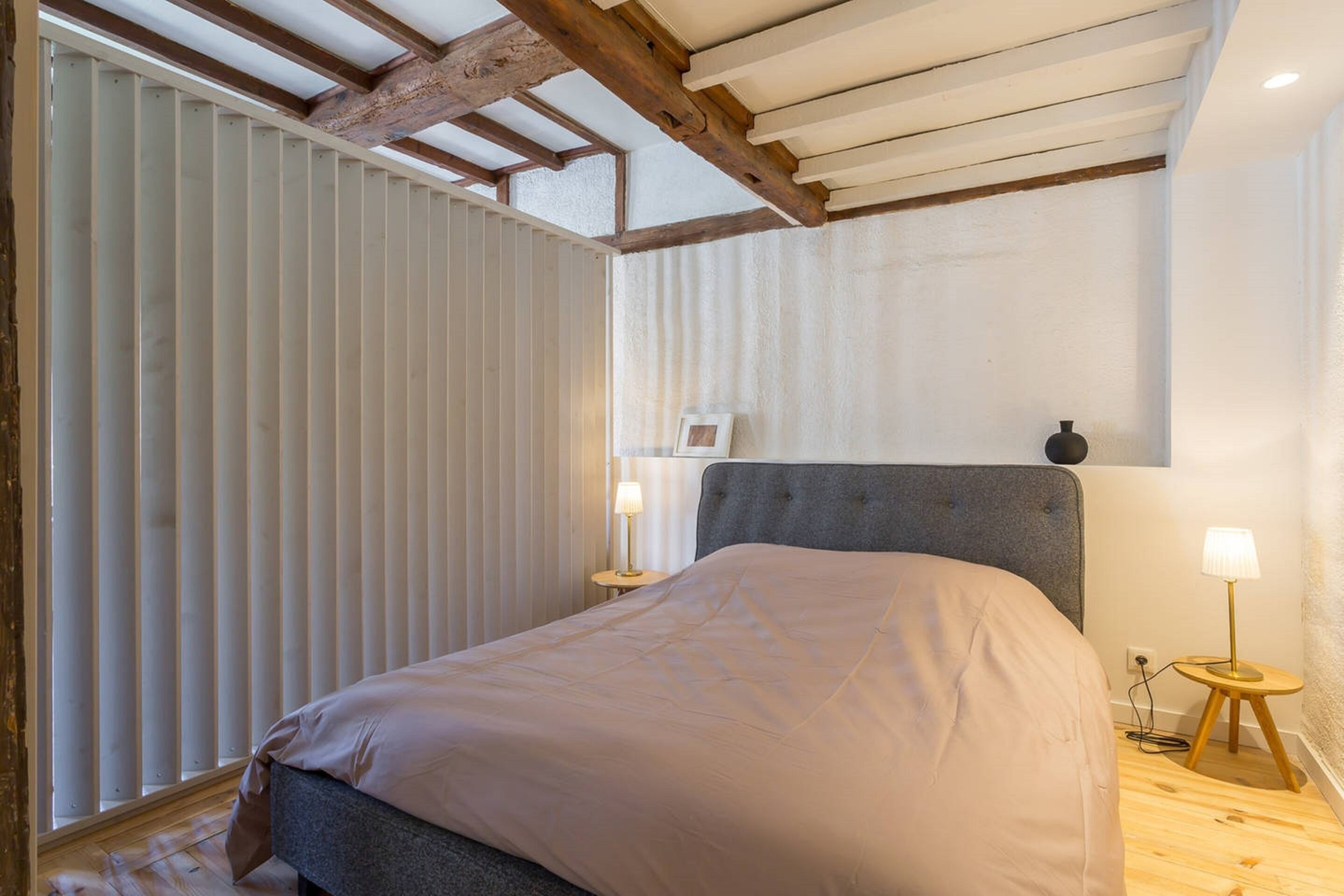 A bedroom with a bed, wooden floor, and a sloped ceiling with exposed beams.