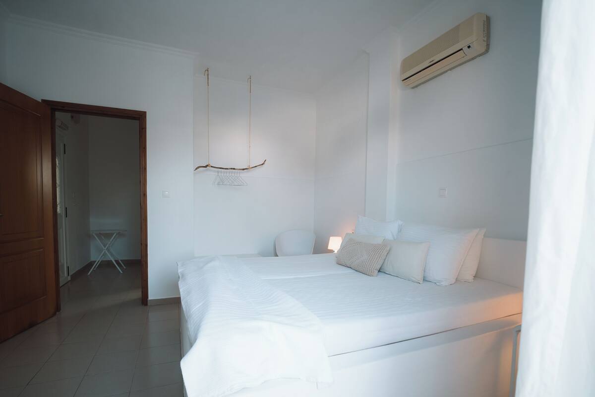 A bedroom with a bed, a hanging light fixture, and a wall-mounted air conditioner.