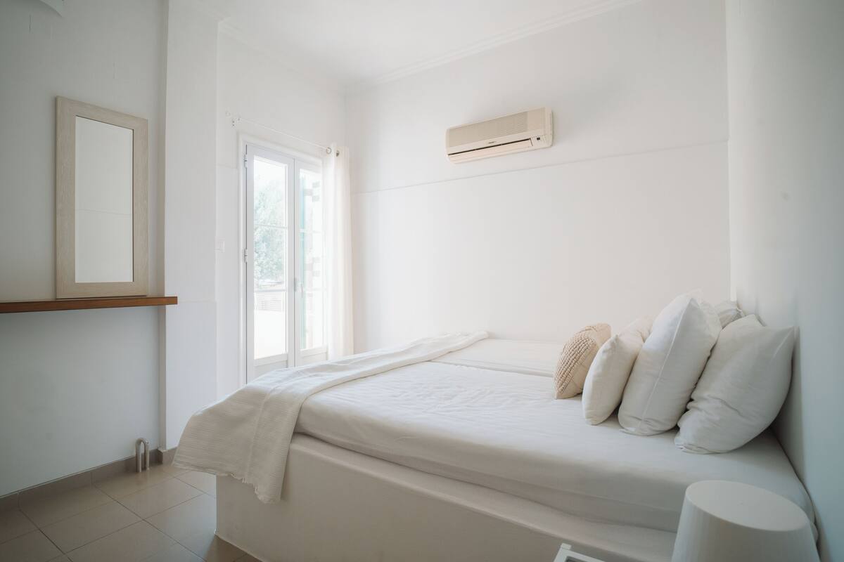 A minimalist bedroom with a bed, a window, and a wall-mounted air conditioner.