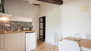 A compact kitchen with a dishwasher, a microwave, and a sink. There is a dining area with a table and chairs, and a clock on the wall. - Cozy cocoon on the heights of Old Lyon (Lyon)