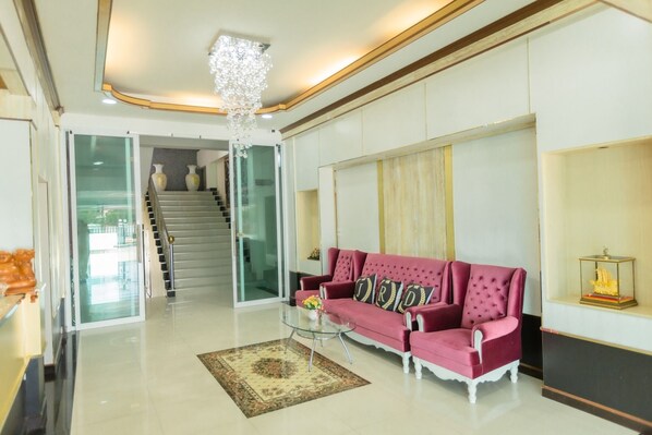 A spacious living area with a red sofa, a glass coffee table, and a chandelier. - JRD Grand Place (Lop Buri)