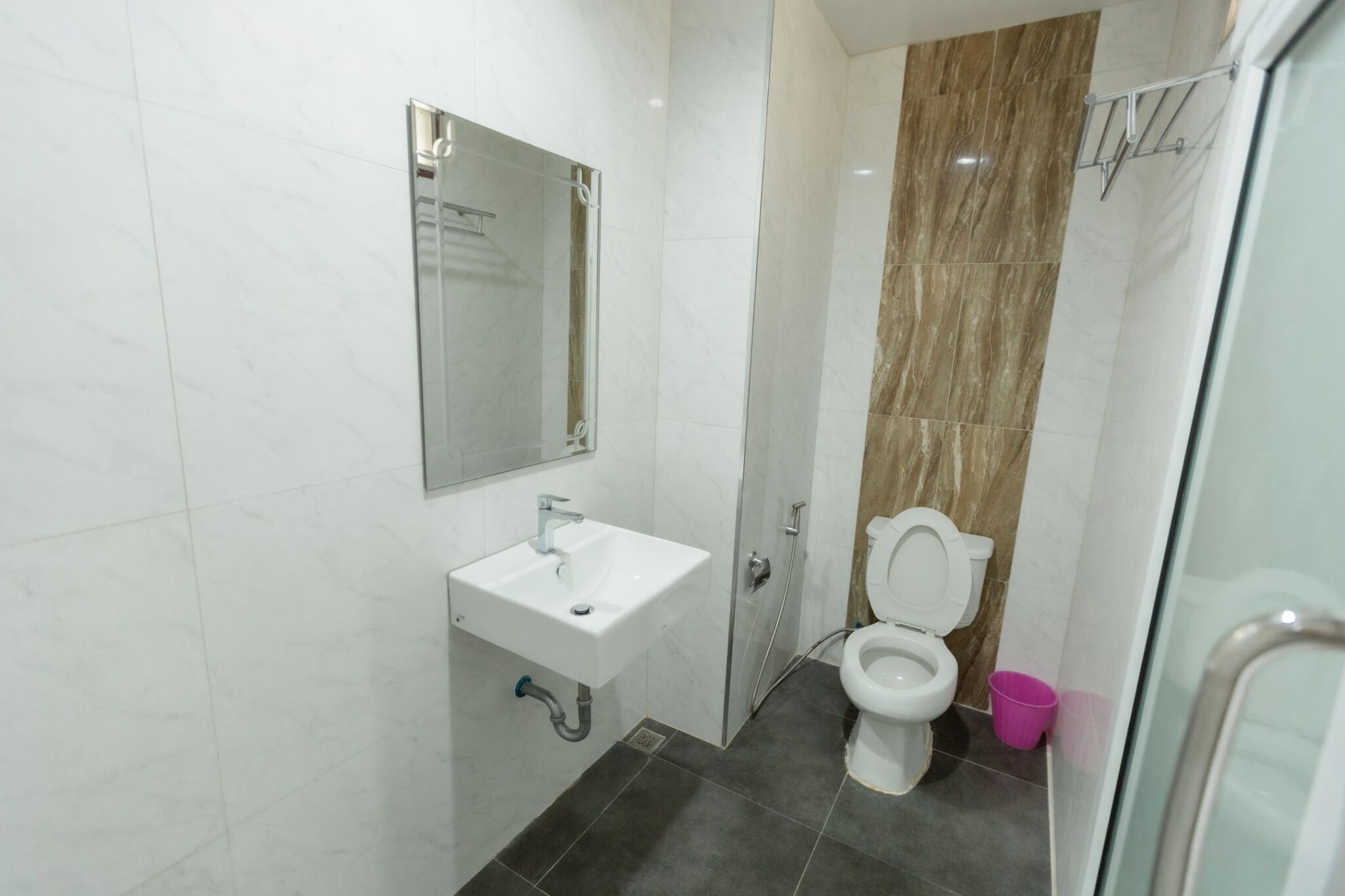 Un baño moderno con lavamanos blanco, espejo, inodoro y zona de ducha.