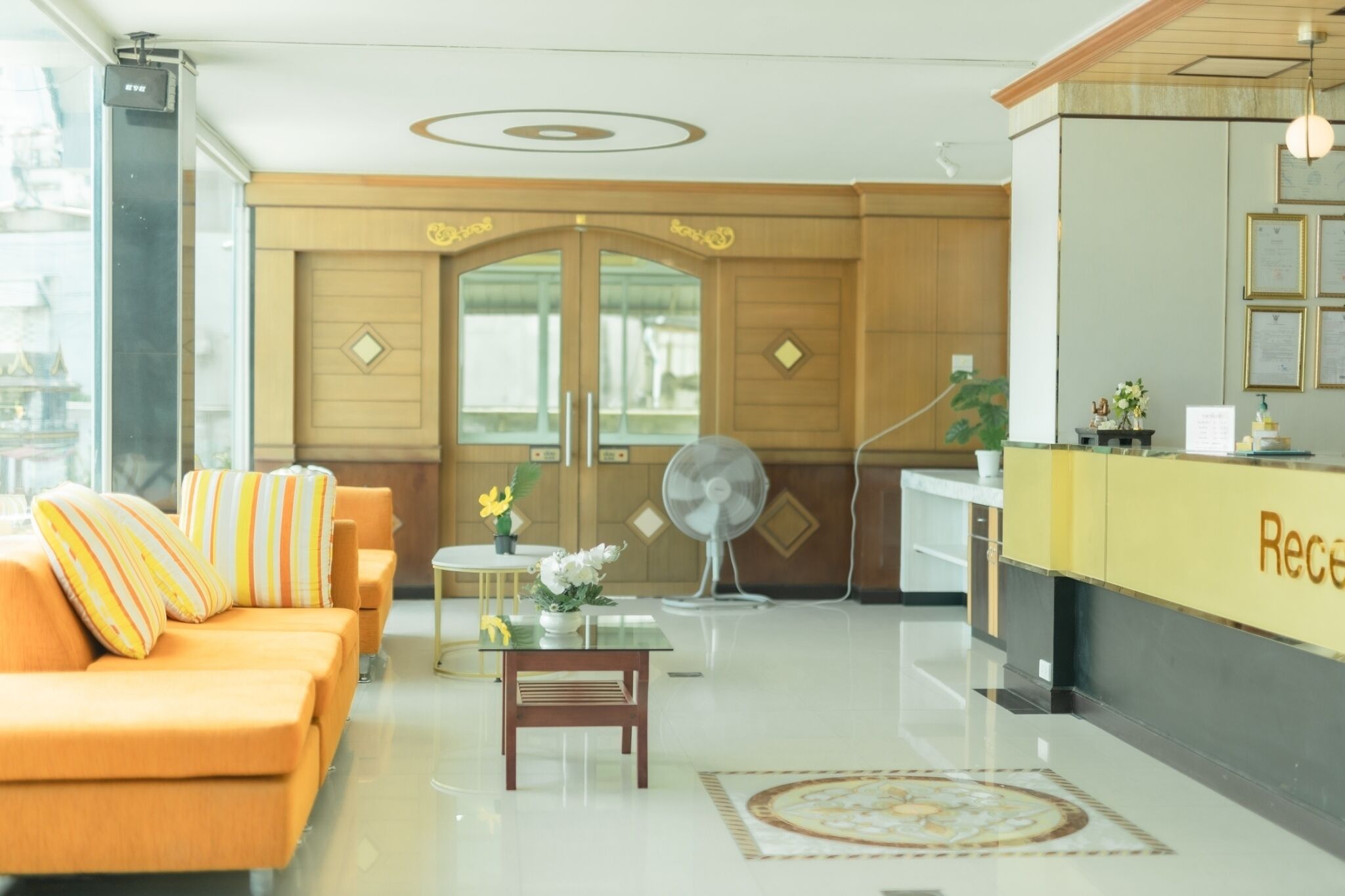 A reception area with a reception desk, a fan, a sofa with striped cushions, and a table with a vase of flowers.