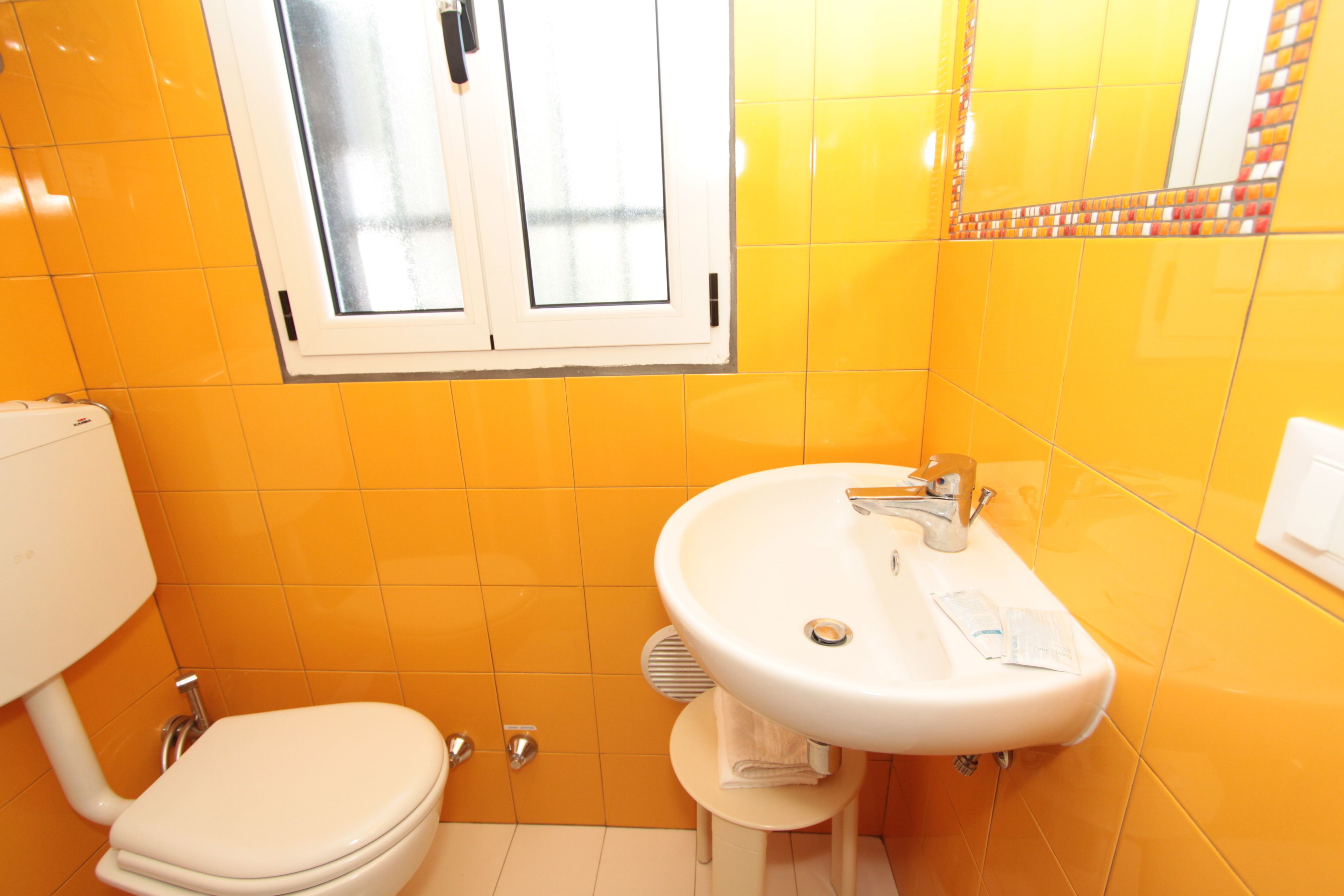 Une salle de bain avec des carreaux jaunes, un lavabo blanc et des toilettes.