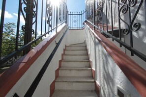 Una escalera con peldaños blancos y bordes rojos, que conduce a una entrada con portón.