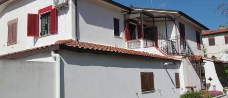 A two-story house with a white exterior, red shutters, and a tiled roof.