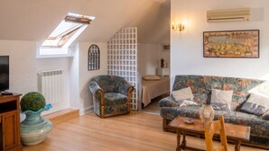 A cozy living room with a sofa, armchair, and a small table. There is a TV stand, a decorative vase, and a ceiling light fixture. - Homerez - Apartment in Lourdes (Lourdes)