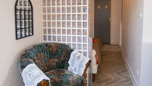 A room with a floral-patterned armchair, a white lace doily, a patterned partition, a door with a light switch, and a herringbone-patterned floor. - Homerez - Apartment in Lourdes (Lourdes)