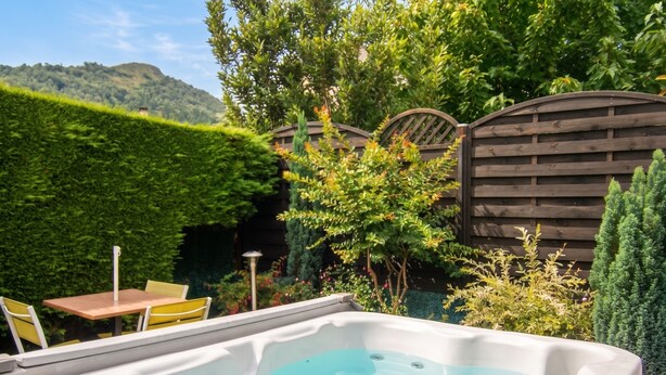 A hot tub in a garden with a wooden fence, a table, and chairs. - Homerez - Apartment in Lourdes (Lourdes)