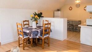 A compact kitchen with a dining area, wooden chairs, a table with a patterned tablecloth, a potted plant, and a clock on the wall. - Homerez - Apartment in Lourdes (Lourdes)
