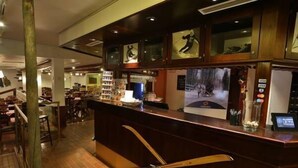 A bar area with wooden counter, framed pictures, and a digital screen. - Ylläs Lake hotel (Kolari)