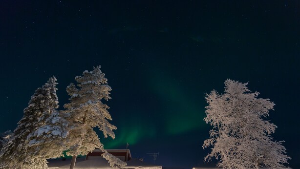 A hotel with a snow-covered exterior, a visible entrance, and a view of the night sky with the aurora borealis. - Ylläs Lake hotel (Kolari)
