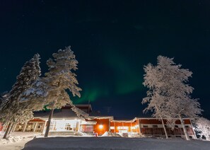 A hotel with a snow-covered exterior, a visible entrance, and a view of the night sky with the aurora borealis. - Ylläs Lake hotel (Kolari)